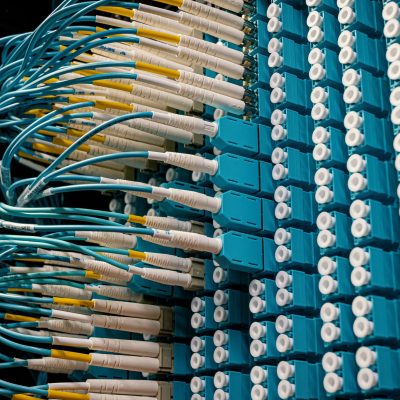 Cabos de fibra óptica conectados a um painel azul em um data center.