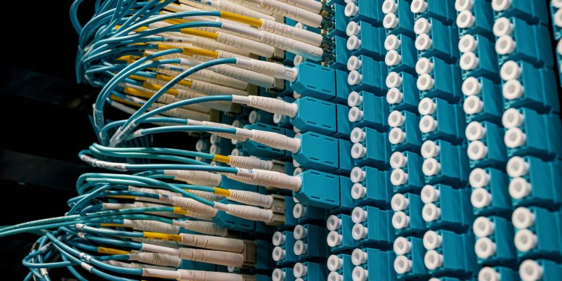 Cabos de fibra óptica conectados a um painel azul em um data center.
